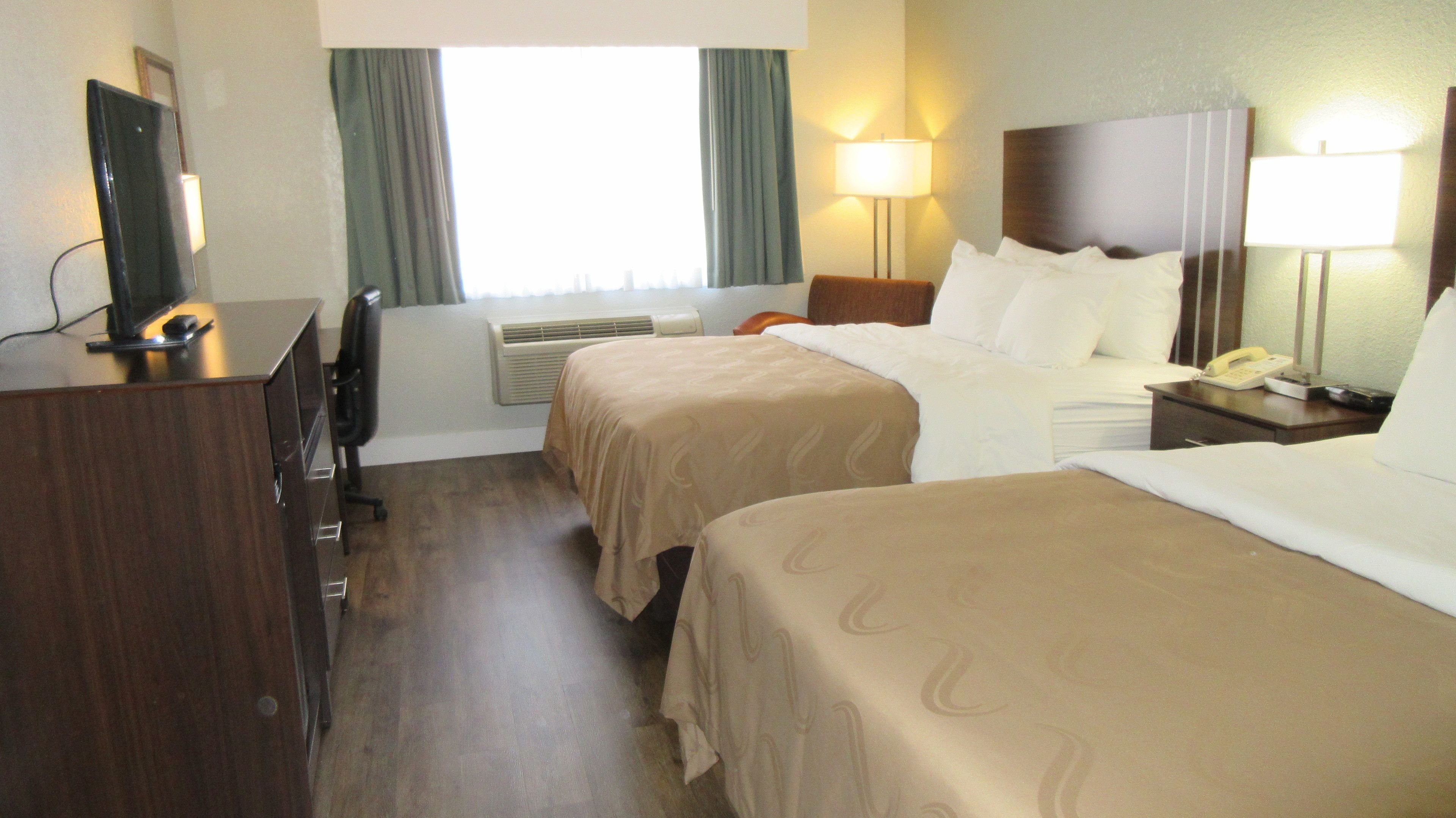 A hotel room with two beds, a desk, a chair, a TV, and a window with curtains.