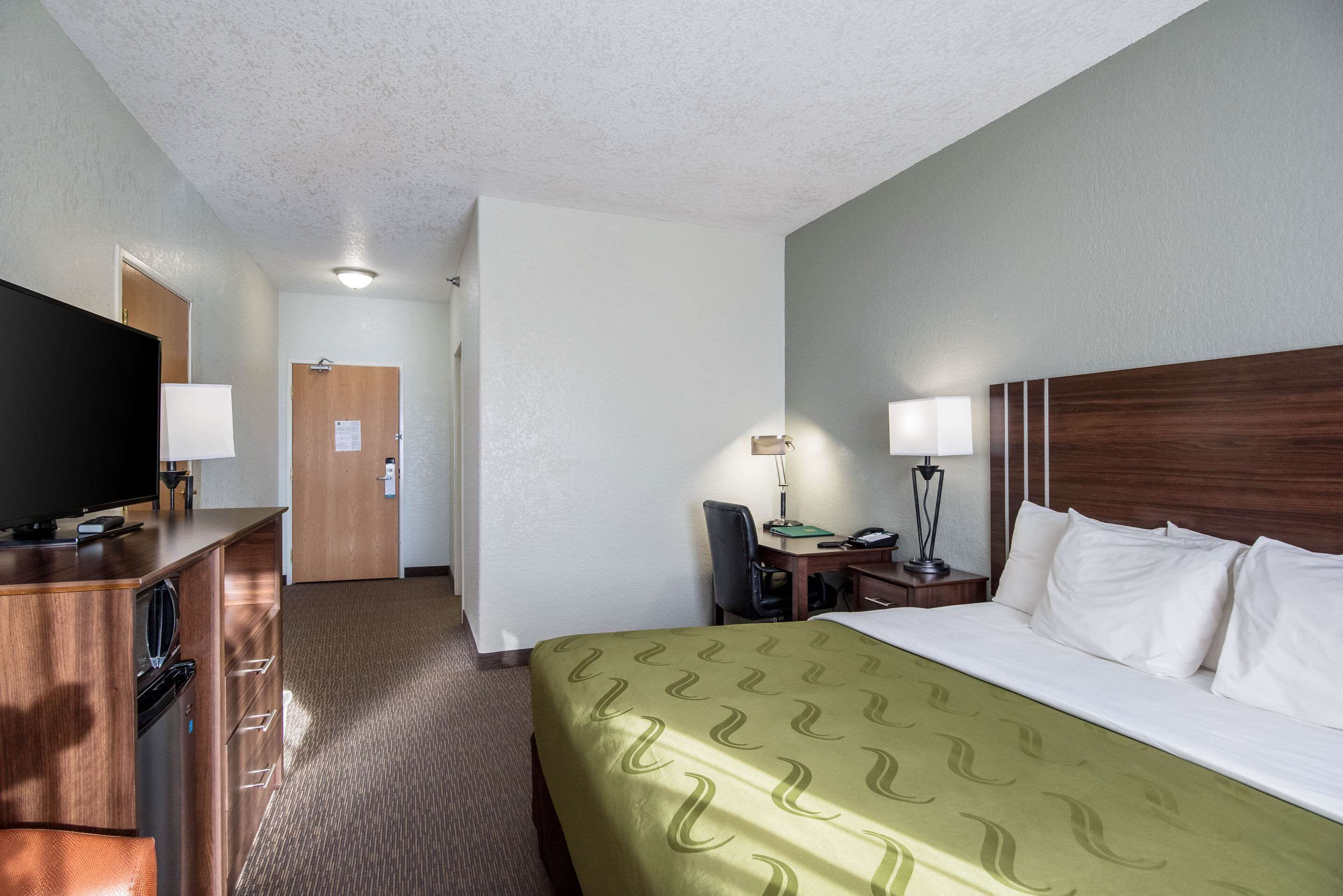 A hotel room with a bed, a desk, a television, and a desk lamp.
