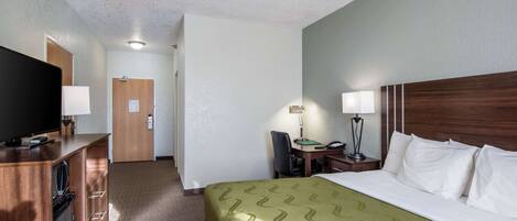 A hotel room with a bed, a desk, a television, and a desk lamp.