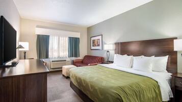 A hotel room with a large bed, a desk, a TV, a sofa, and a window with curtains.