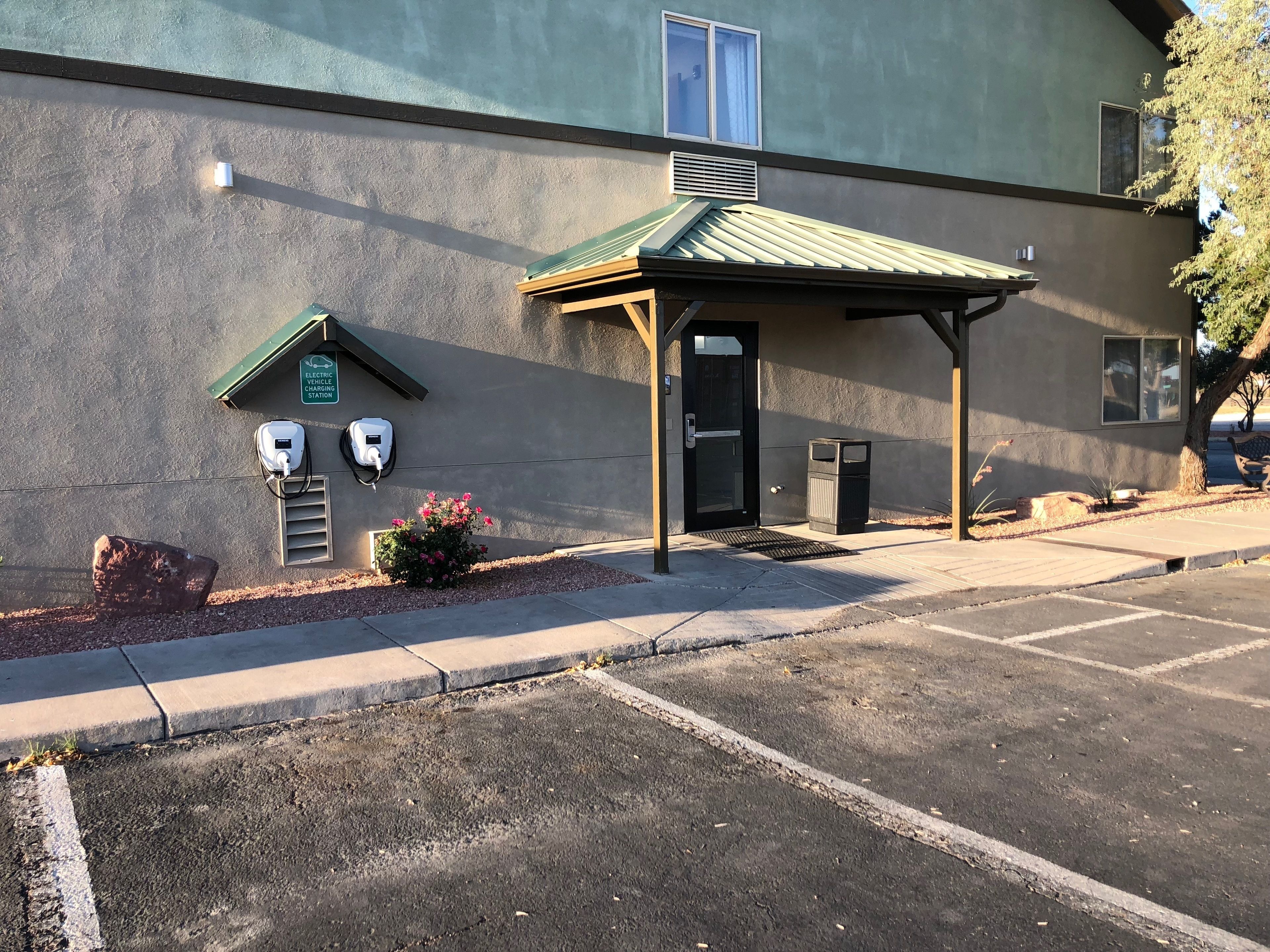 A building with a parking lot, a covered entrance, electric vehicle charging stations, and a small garden area.