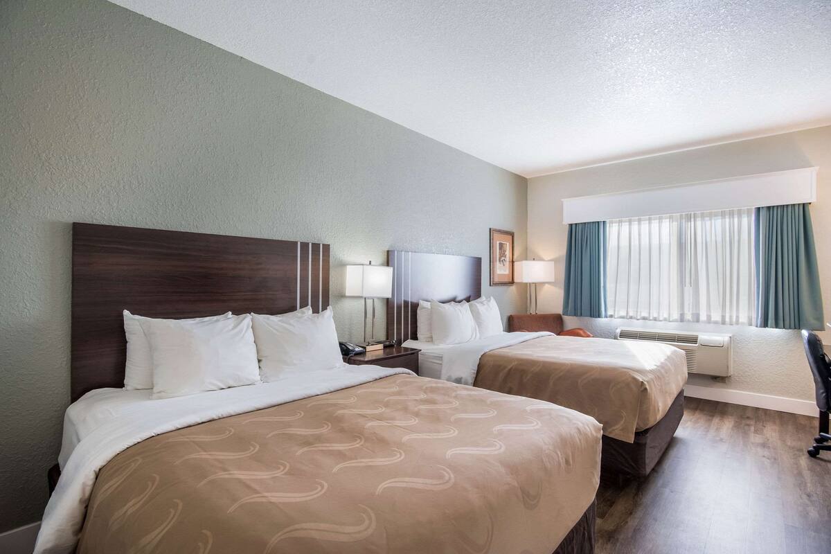 A hotel room with two beds, a desk, a chair, and a window with curtains.