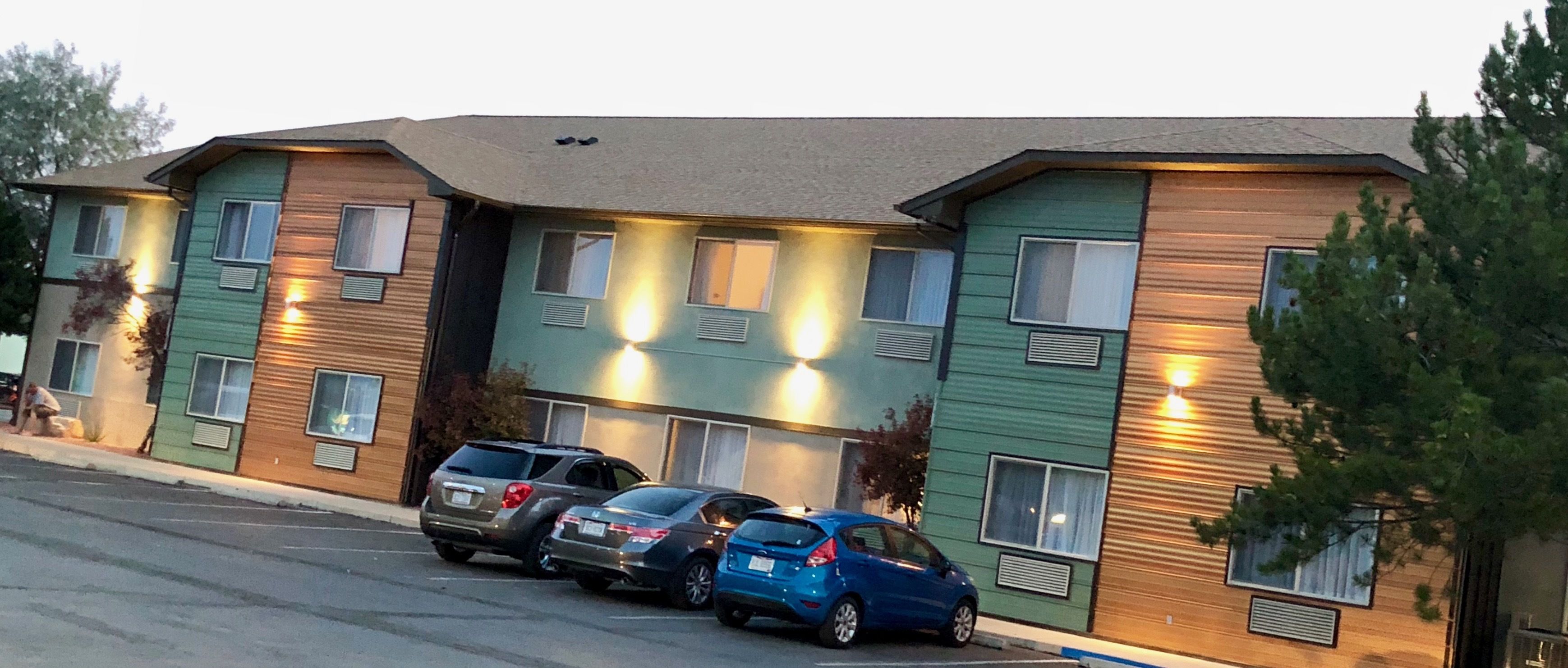 A multi-story building with several parking spaces and a row of parked cars.