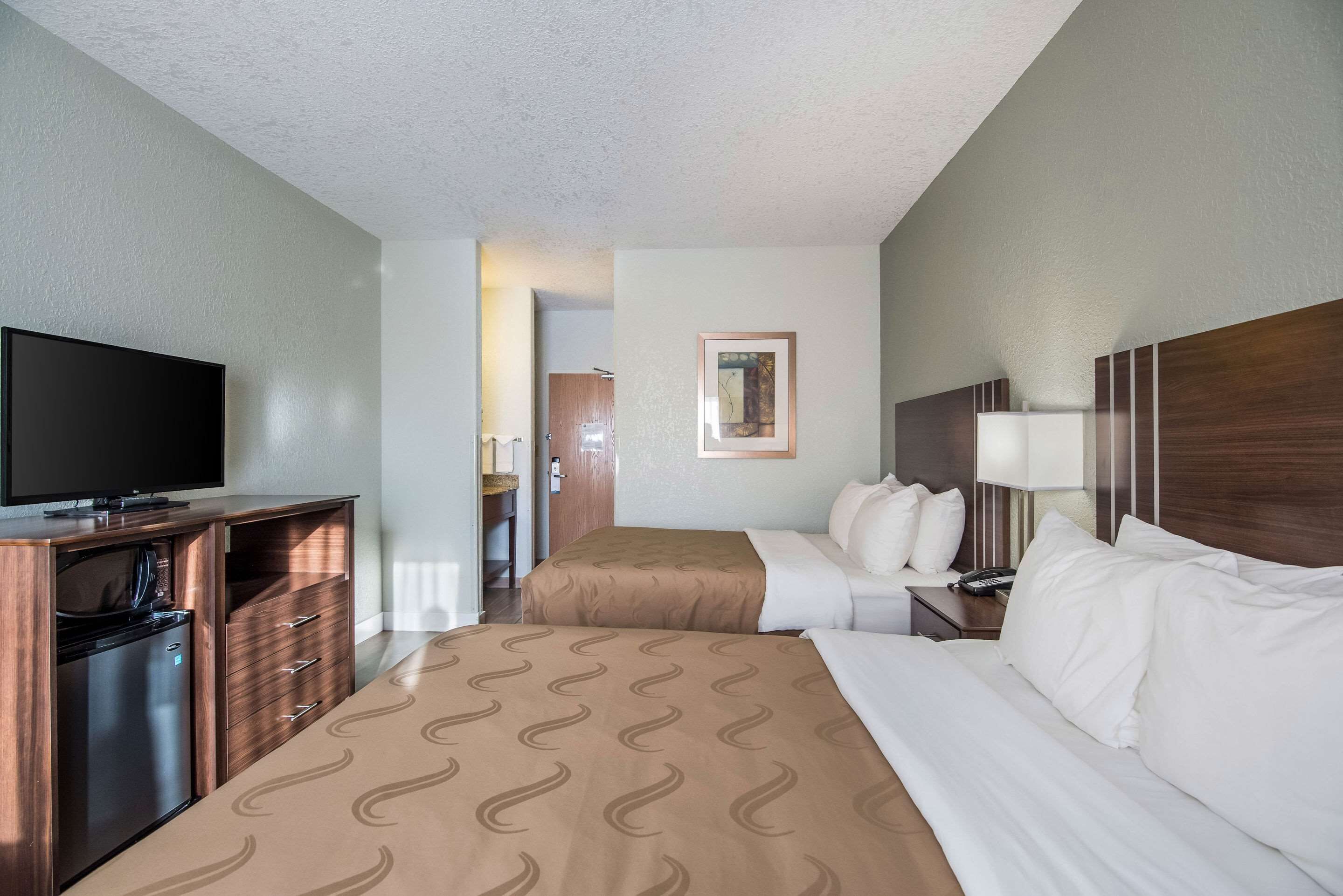 A hotel room with a bed, a TV, a desk, and a bathroom.
