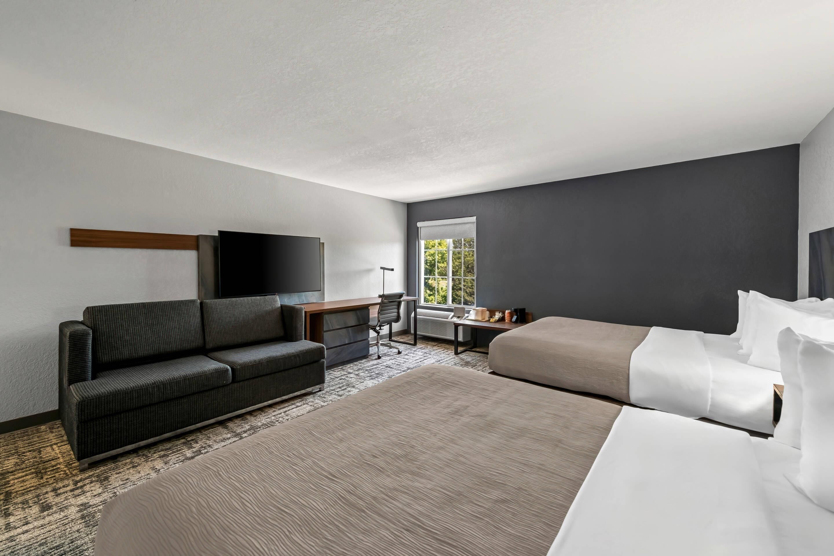 Una camera d'albergo moderna con un letto grande, un divano, una scrivania e una TV.