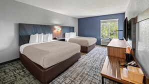 A hotel room with two beds, a desk, a coffee maker, and a TV.