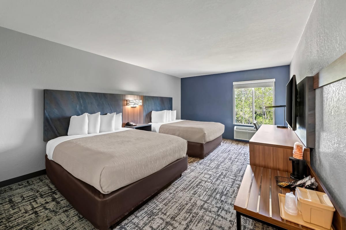 Ein Hotelzimmer mit zwei Betten, einem Schreibtisch, einer Kaffeemaschine und einem Fernseher.