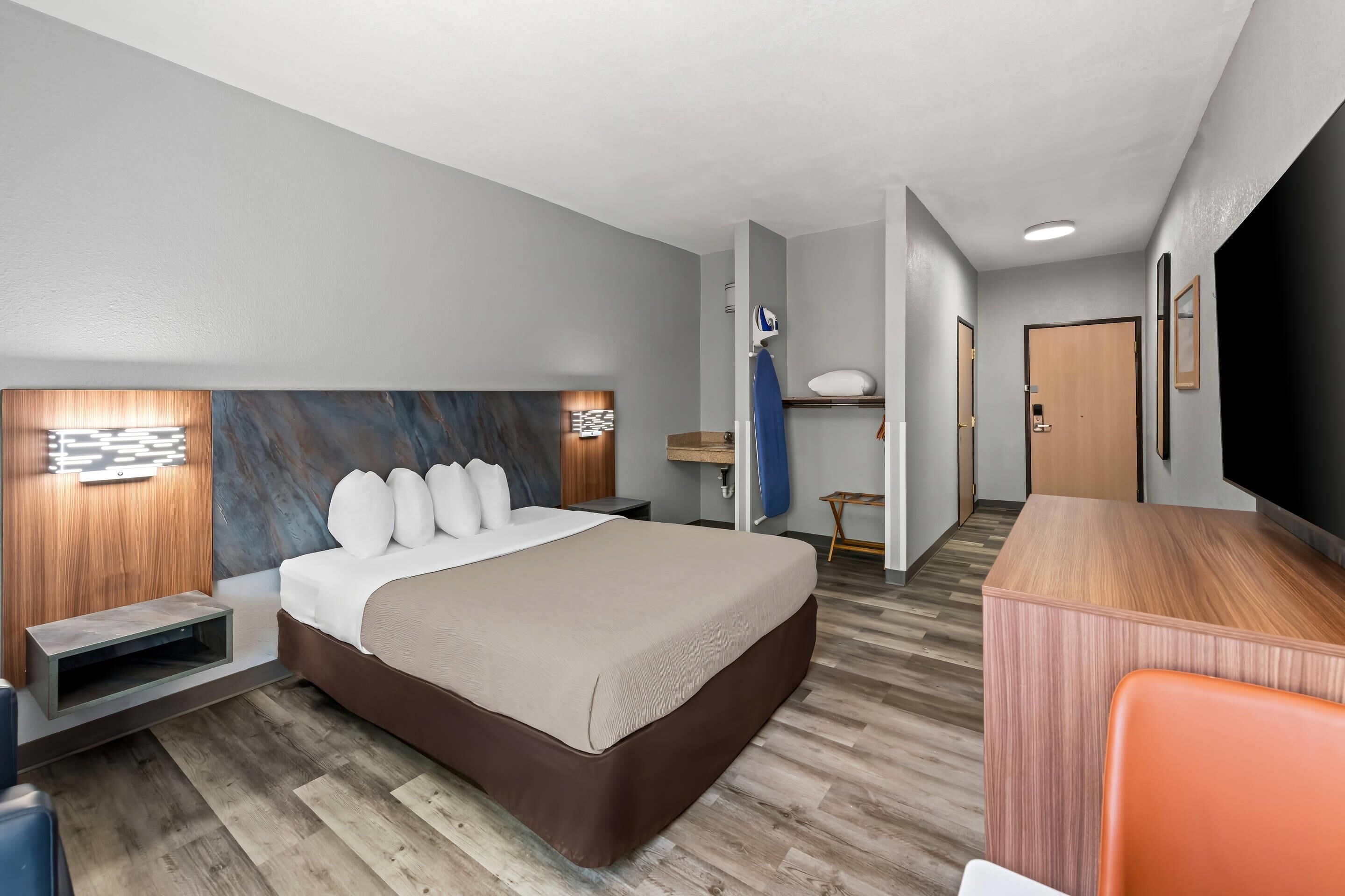 Una habitación de hotel moderna con una cama grande, cabecera de madera y un pequeño escritorio.
