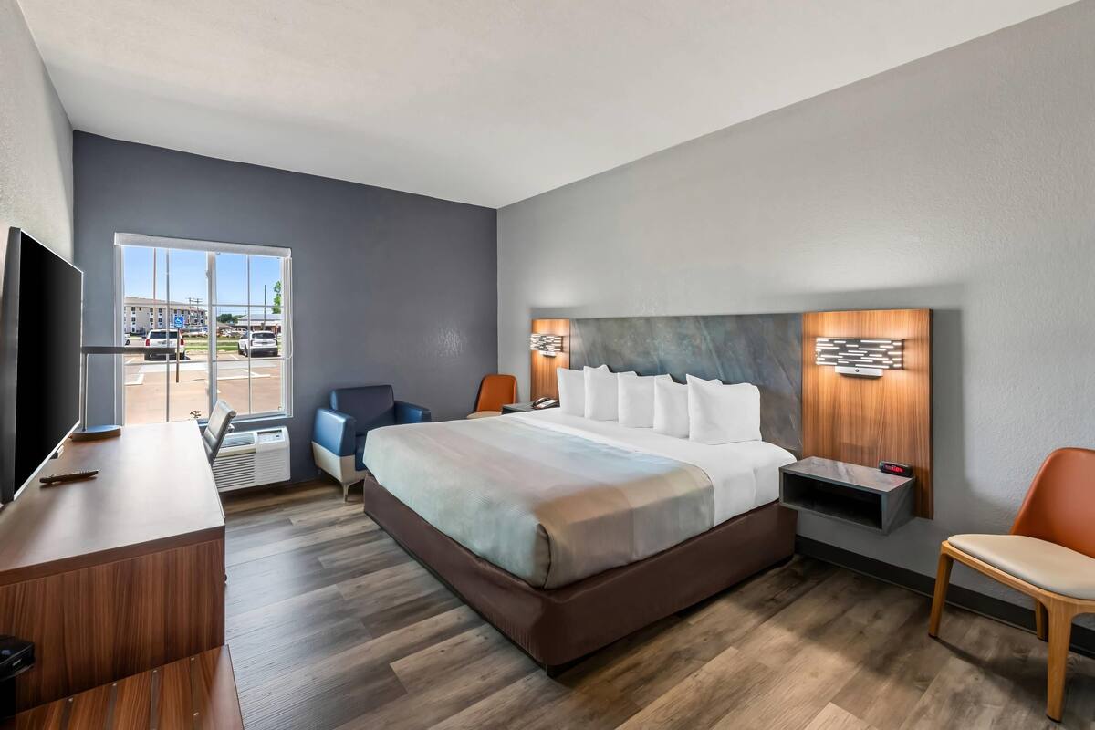 A modern hotel room with a large bed, a desk, a chair, and a TV.