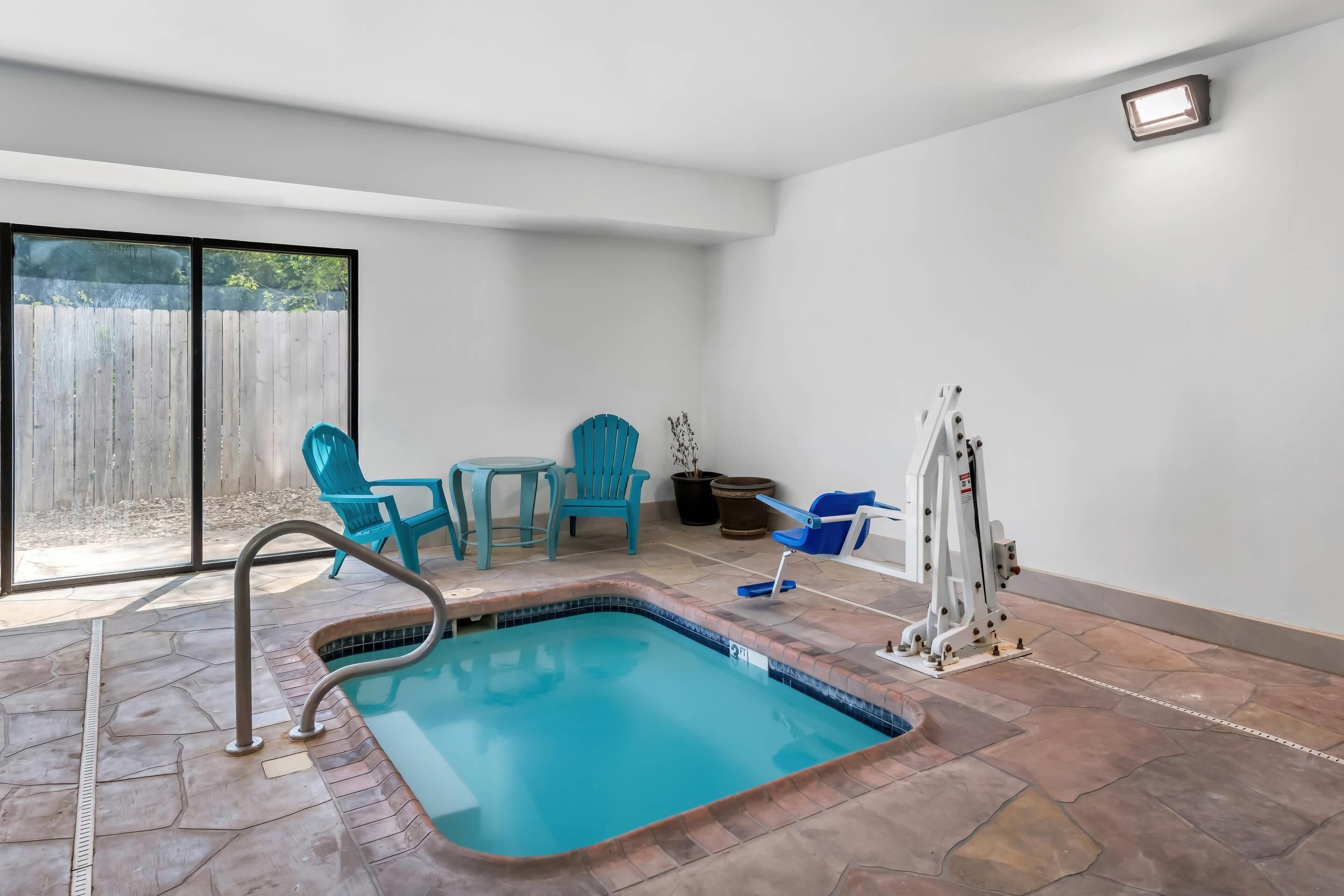 Piscina com deck revestido de azulejos, escada de metal e duas cadeiras azuis.