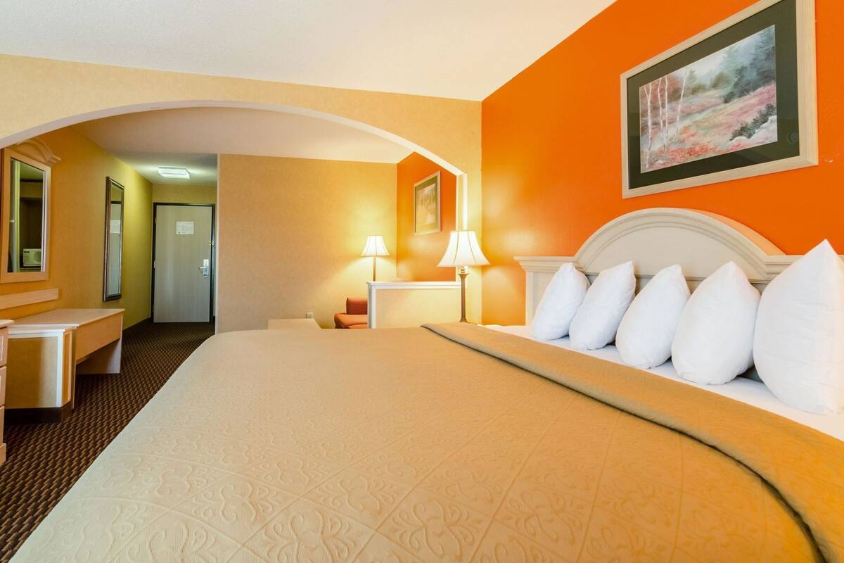 Ett hotellrum med en stor säng, ett skrivbord, en stol och en tavla på väggen.