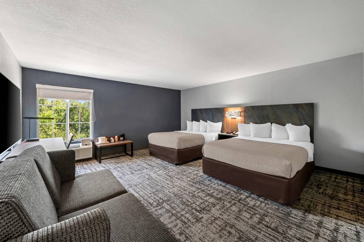 A hotel room with two beds, a sofa, a small table, and a large window.