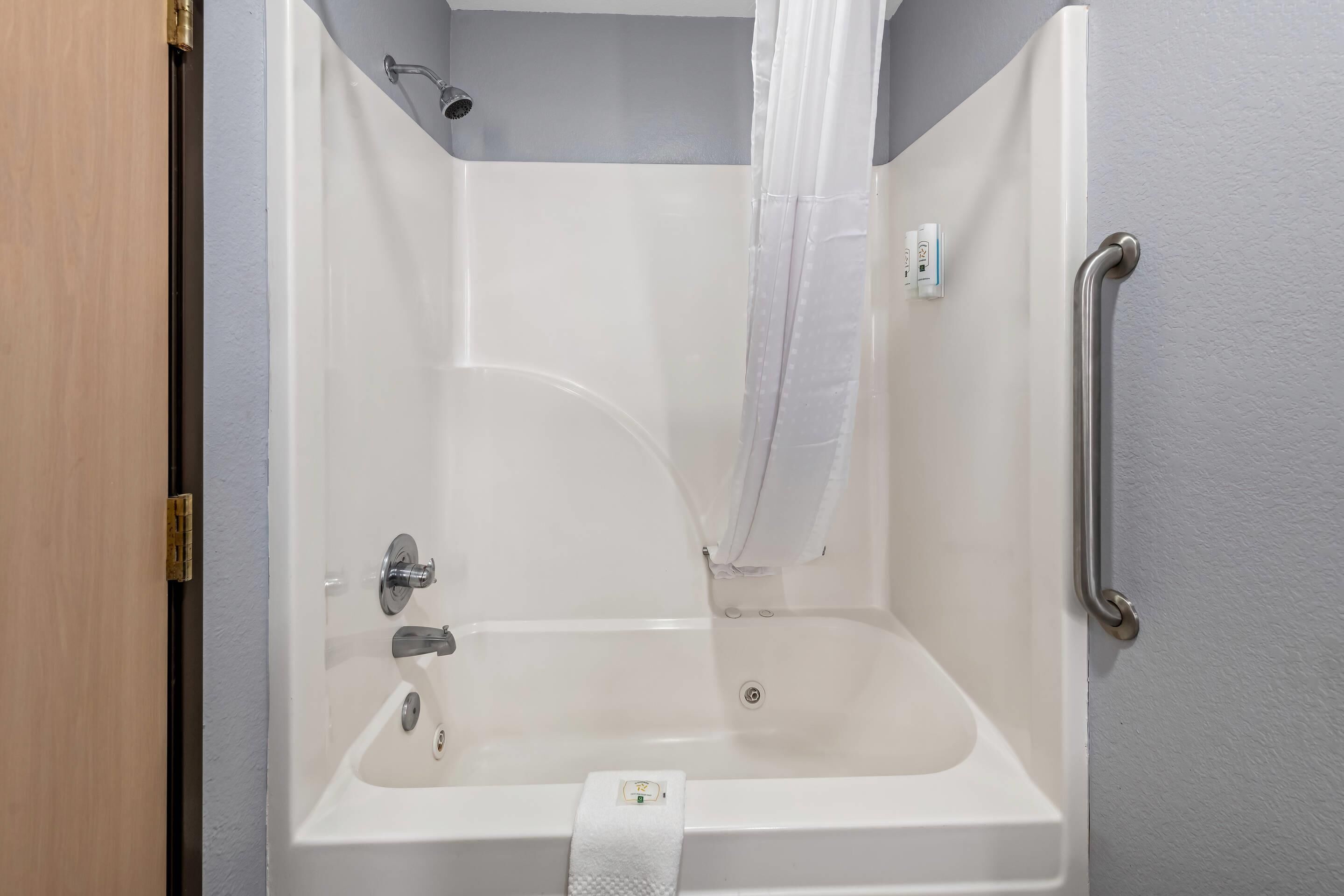 Una bañera blanca con un cabezal de ducha, un pasamanos y una toalla colgada al lado.