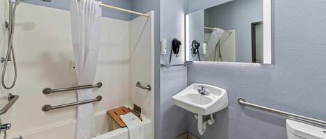 A modern bathroom with a bathtub, shower, and sink, equipped with handrails and a mirror.