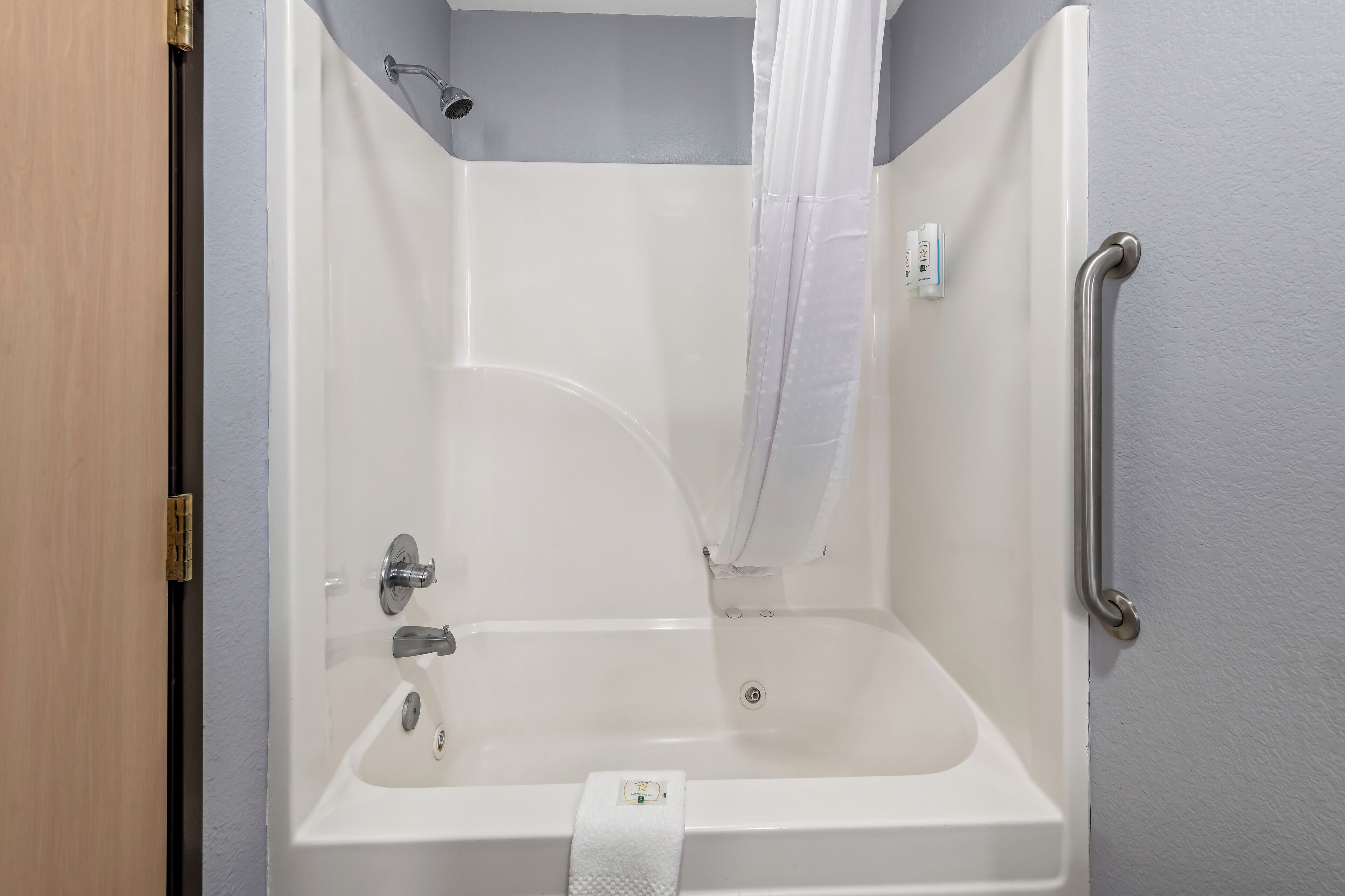 Une baignoire blanche avec un pommeau de douche, une barre d’appui sur le côté droit et une serviette suspendue sur le bord.