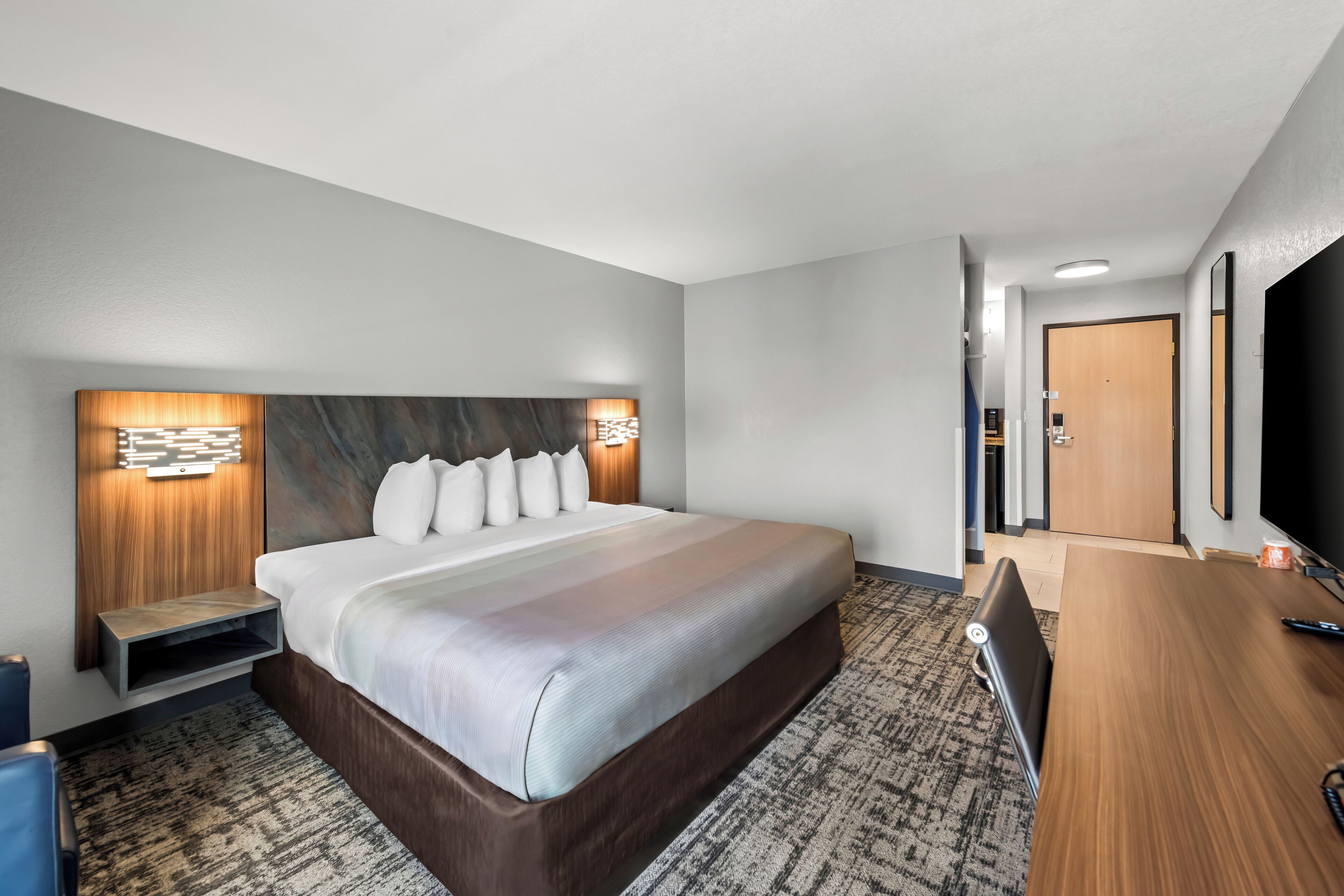 A hotel room with a large bed, a desk, a TV, and a door leading to the bathroom.