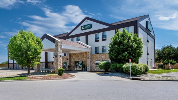 A modern hotel with a stone facade, a covered entrance, and a sign indicating 'Quality' and 'Comfort'.