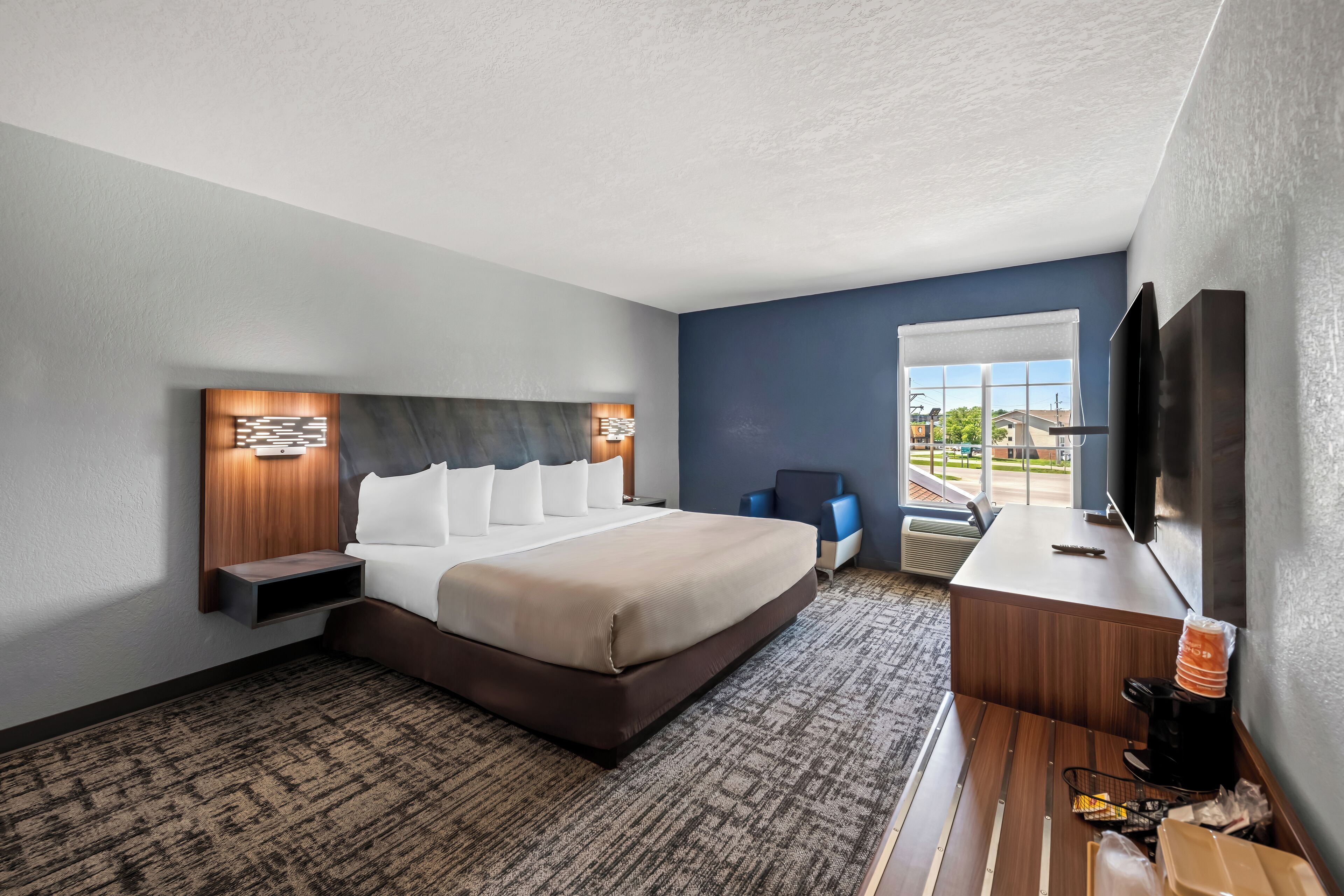 A hotel room with a large bed, a desk with a flat-screen TV, and a window with a view of the outdoors.