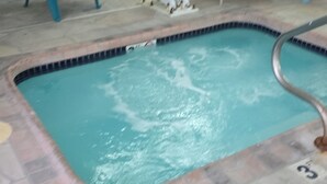 A swimming pool with a tiled deck, a ladder, and several blue chairs around it.
