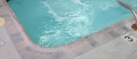 A swimming pool with a tiled deck, a ladder, and several blue chairs around it.