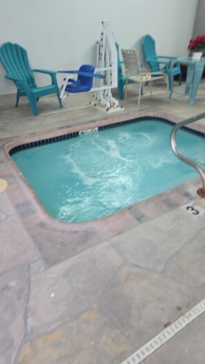 A swimming pool with a tiled deck, a ladder, and several blue chairs around it.