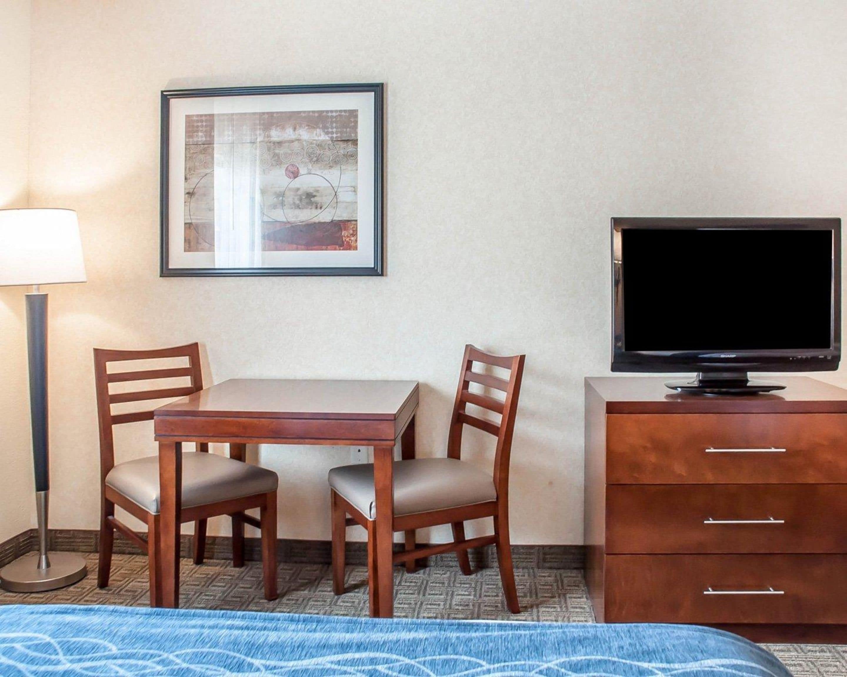 Ein Hotelzimmer mit einem Bett, einem Schreibtisch mit zwei Stühlen, einem Fernseher auf einer Holzkommode und einem gerahmten Bild an der Wand.