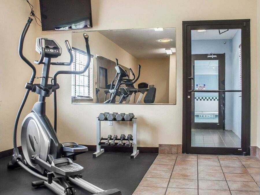 A gym with cardio equipment, dumbbells, and a mirror reflecting the room.
