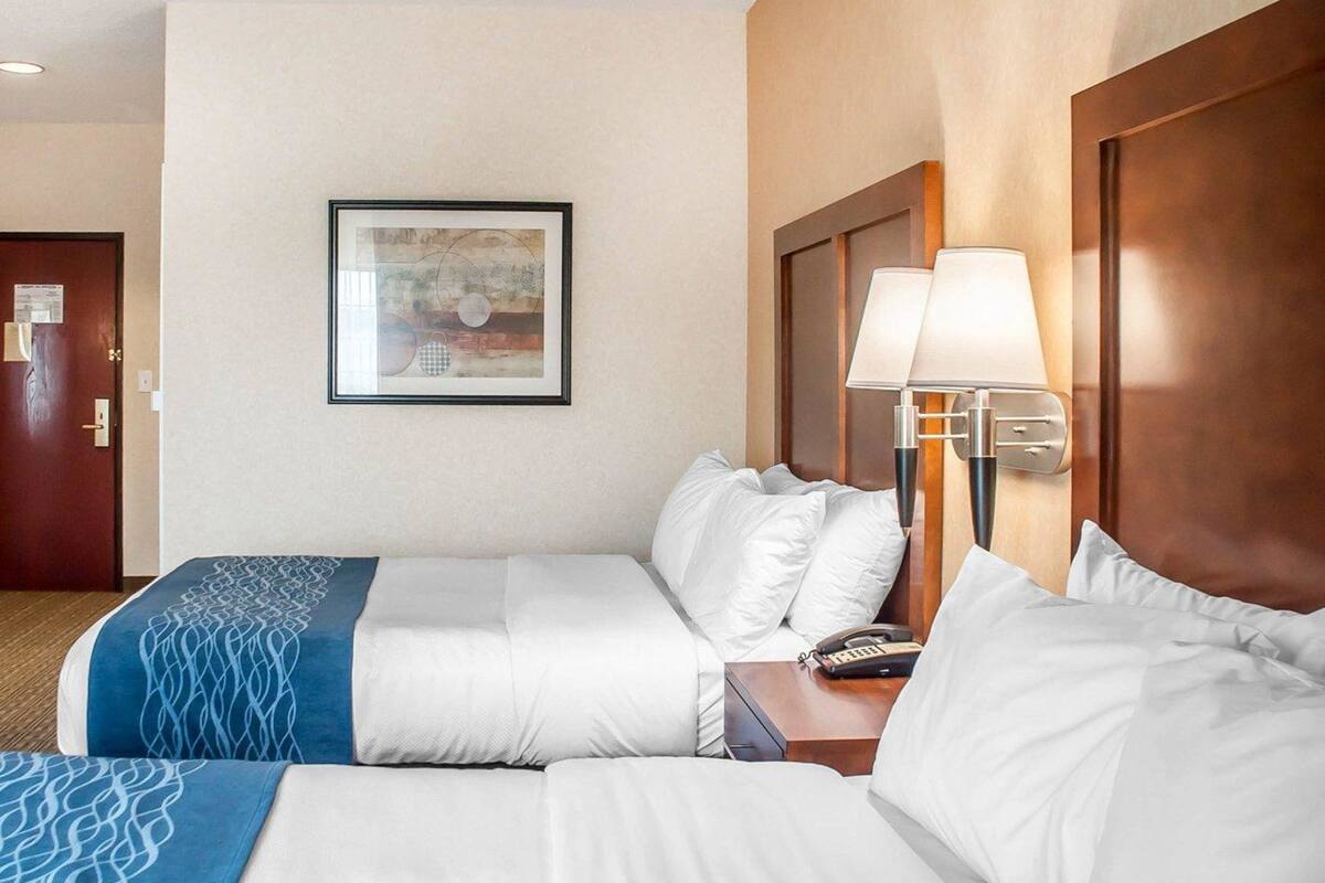 A hotel room with two beds, a framed artwork on the wall, and a bedside lamp.