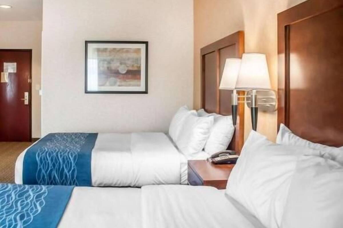 A hotel room with two beds, a framed picture on the wall, a nightstand with a lamp, and a door with a sign.