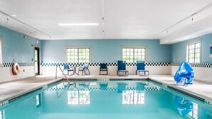 A swimming pool with clear blue water, surrounded by blue chairs and a lifebuoy on the wall.