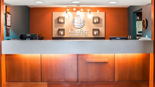 A hotel reception desk with a sign reading "Comfort Inn & Suites," a Dell computer, and a clock on the wall.