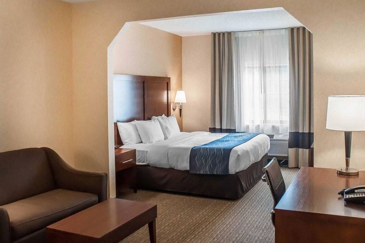 A hotel room with a bed, a desk, a chair, a lamp, and a window with curtains.