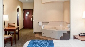A hotel room with a bed, a desk, a chair, a desk lamp, a telephone, and a bathroom with a bathtub and a toilet.