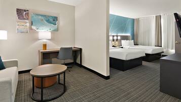A hotel room with a bed, a desk with a chair, a small table, and artwork on the wall.