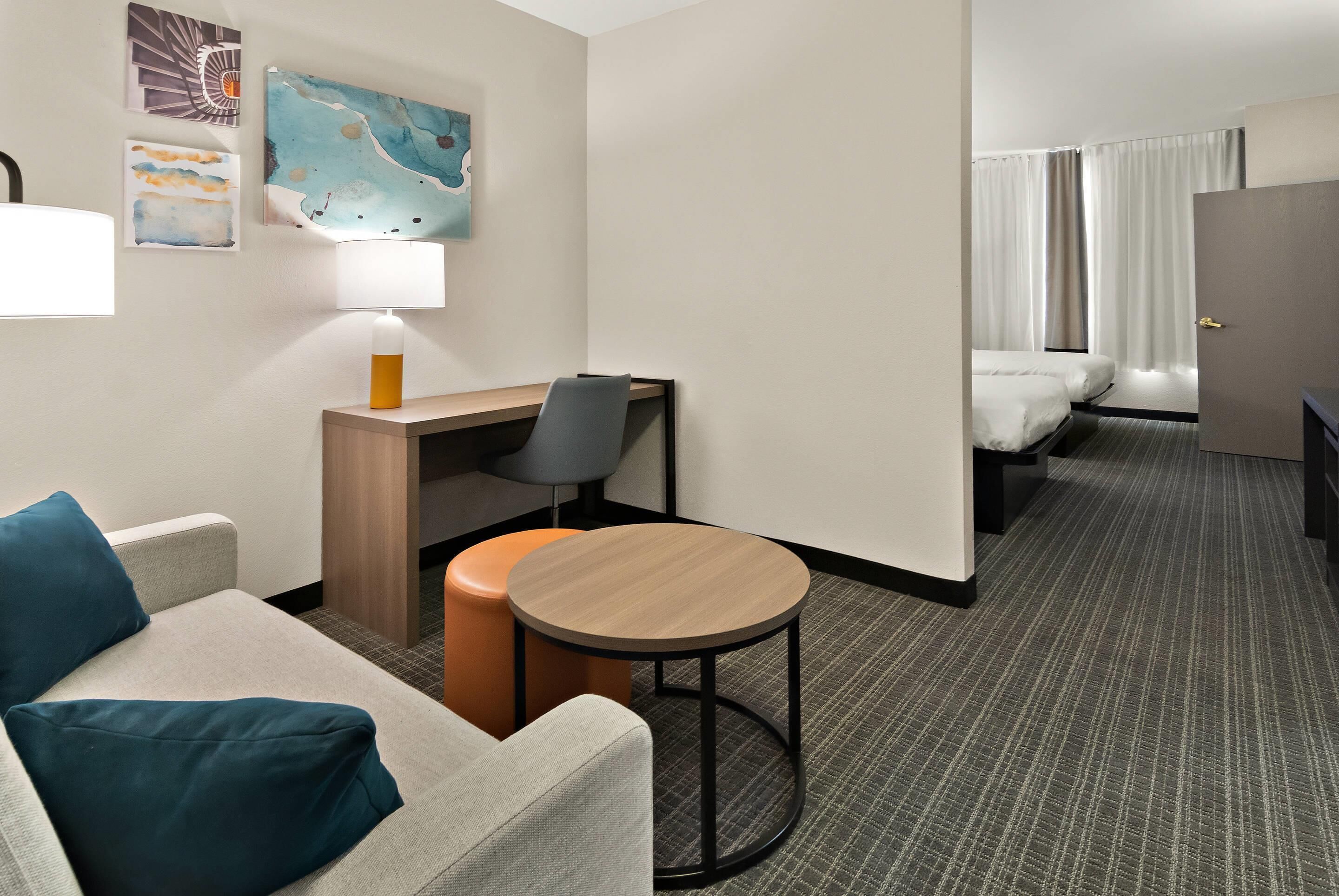 Habitación de hotel con sofá, una mesita redonda, escritorio, silla, lámpara y cama.
