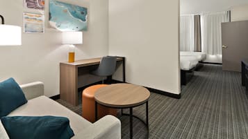 Habitación de hotel con sofá, una mesita redonda, escritorio, silla, lámpara y cama.
