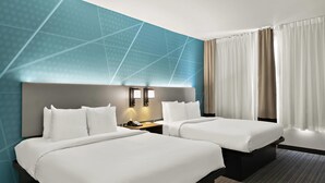 Quarto de hotel com duas camas, uma mesa de cabeceira com telefone e parede com padrões geométricos.