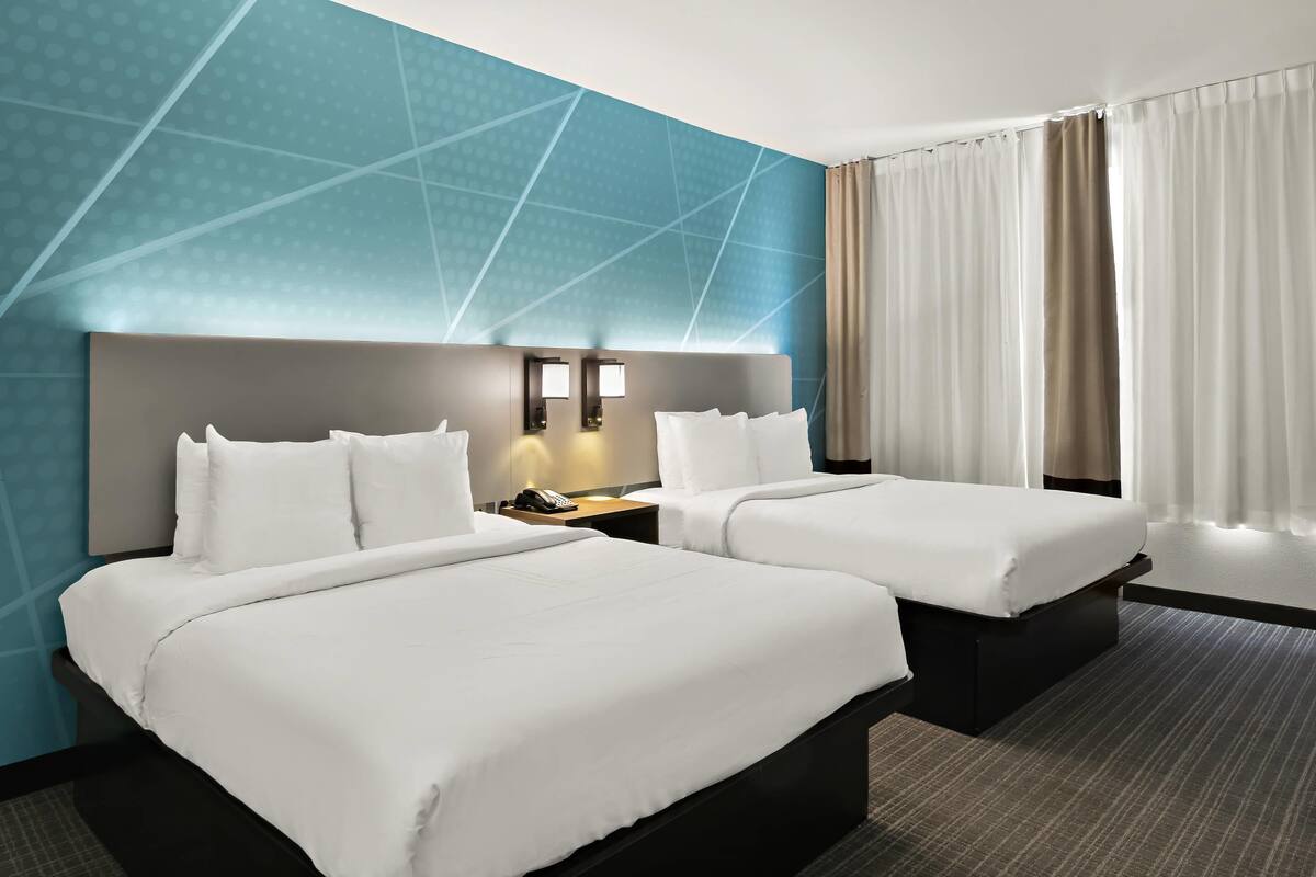Una habitación de hotel con dos camas, una mesita de noche con teléfono y una pared con diseños geométricos.