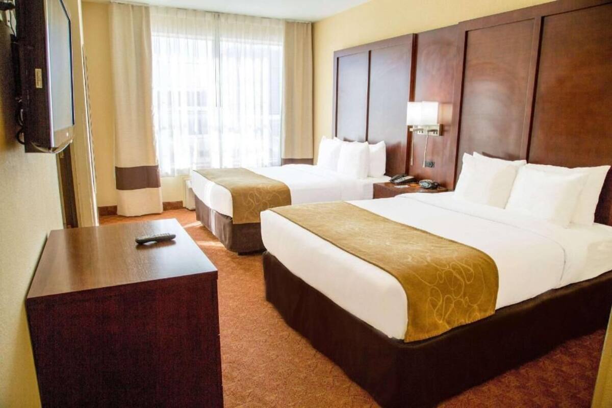 Habitación de hotel con dos camas, televisión, escritorio y mesita de noche.