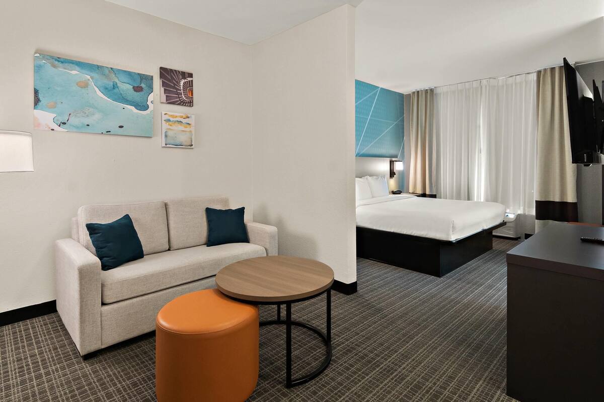 Habitación de hotel con sofá, una mesa redonda, cama y obras de arte en la pared.