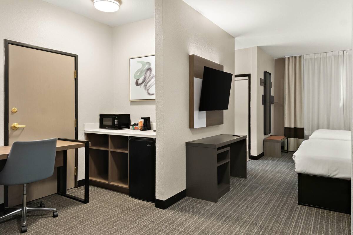 Habitación de hotel con escritorio, silla, cama, televisor y microondas.