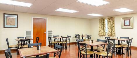 A dining area with multiple tables and chairs, a wooden door, and framed pictures on the walls.