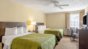 A hotel room with two beds, a desk, a chair, a ceiling fan, and a TV.