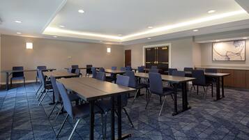 A conference room with multiple tables and chairs, a patterned carpet, recessed ceiling lights, and a large abstract painting on the wall.