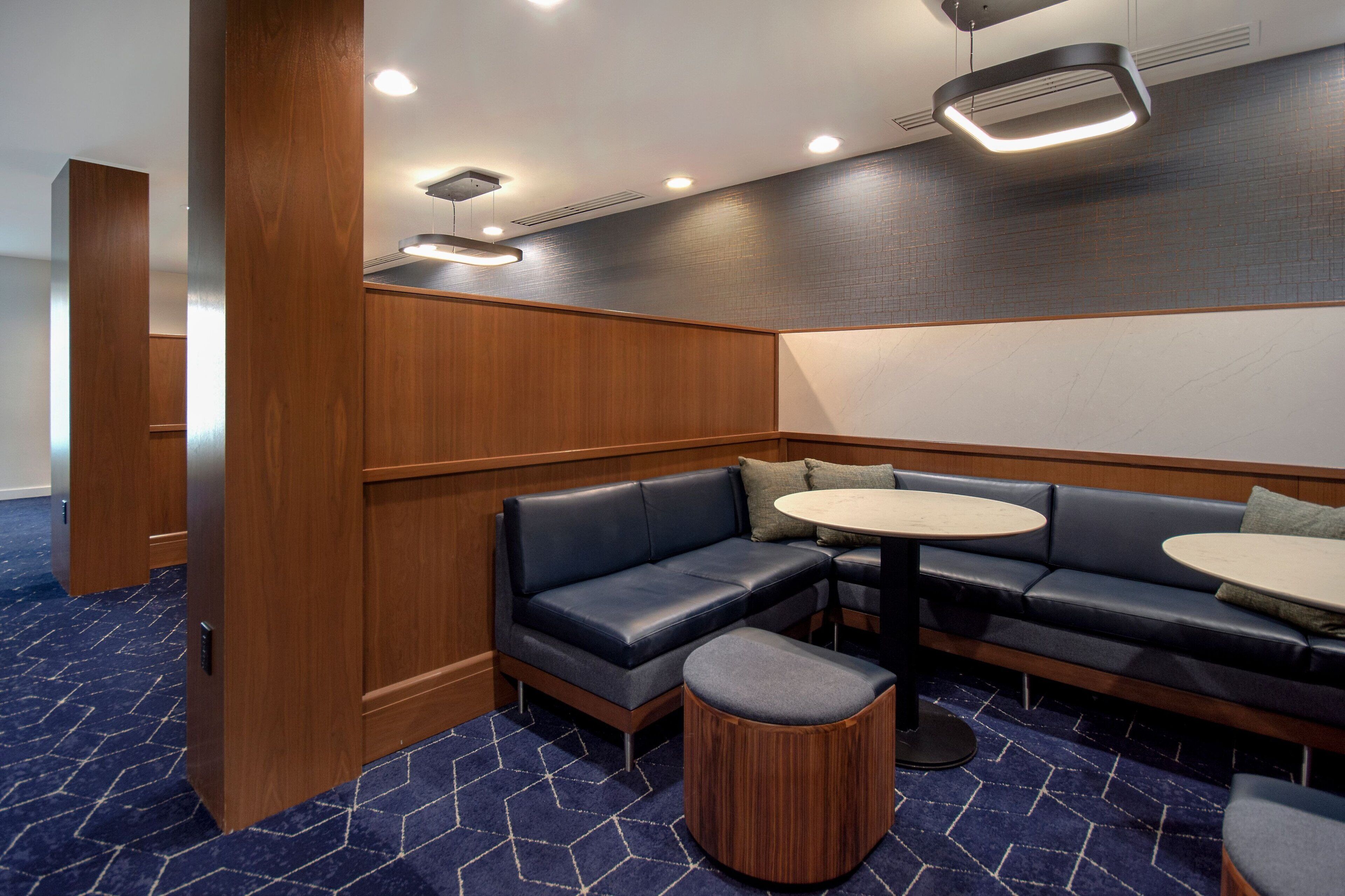 A corner seating area with a dark blue sofa, two round tables, and a wooden accent wall.