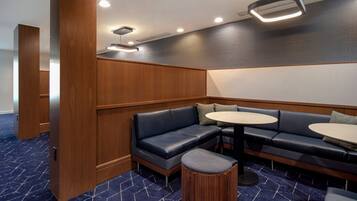 A corner seating area with a dark blue sofa, two round tables, and a wooden accent wall.