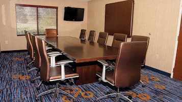 Un salón de conferencias con una mesa grande, seis sillas, un televisor en la pared y alfombra estampada.