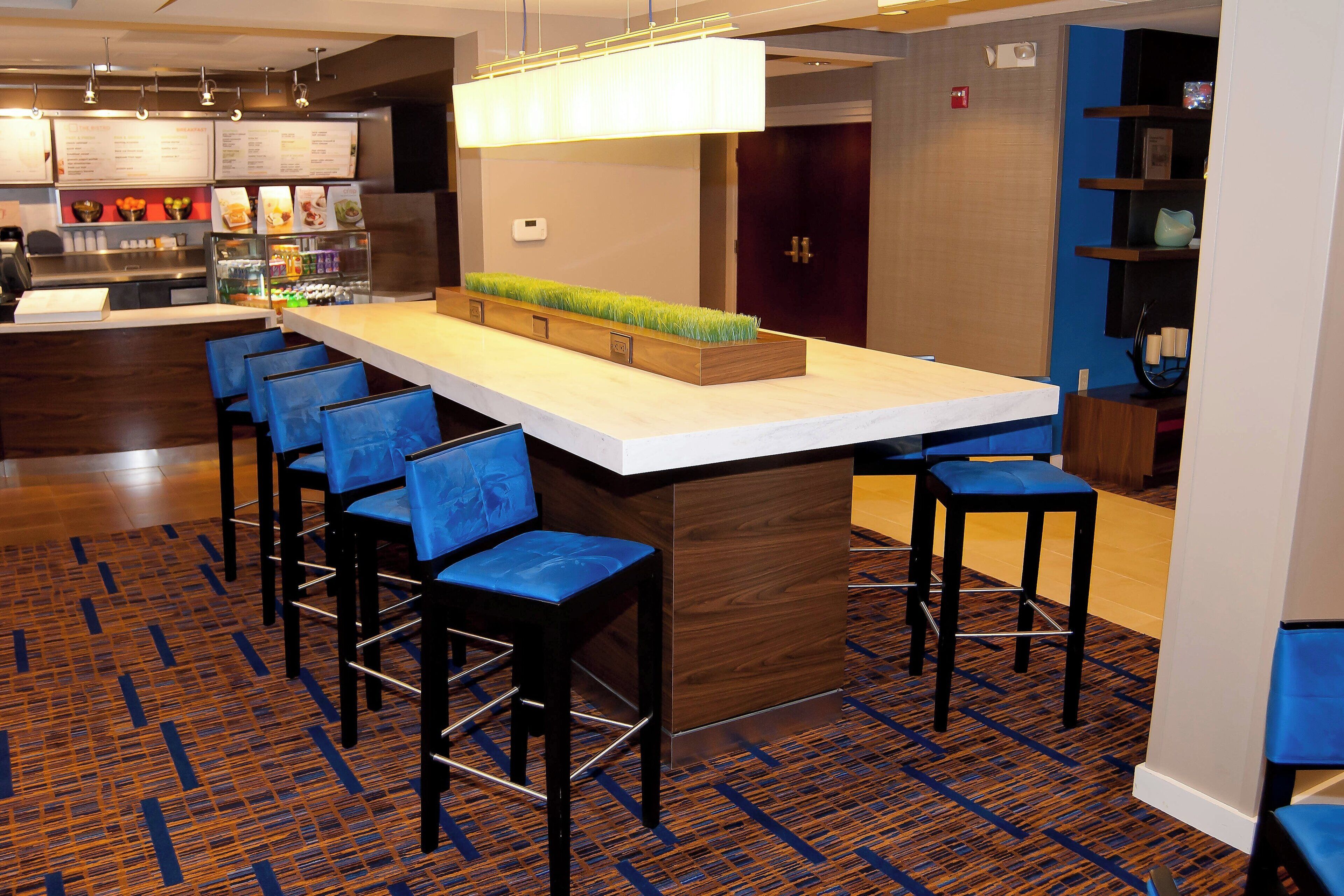 A modern bar area with a long counter, multiple bar stools, and a decorative planter with green plants.