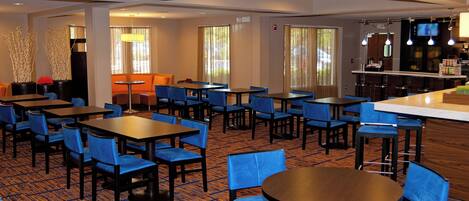 Un comedor de hotel con varias mesas y sillas, una zona de bar y una pantalla de televisión.