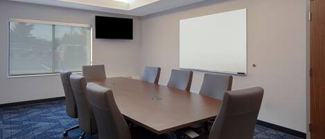 A conference room with a large table, six chairs, a projector screen, a TV, and a door.